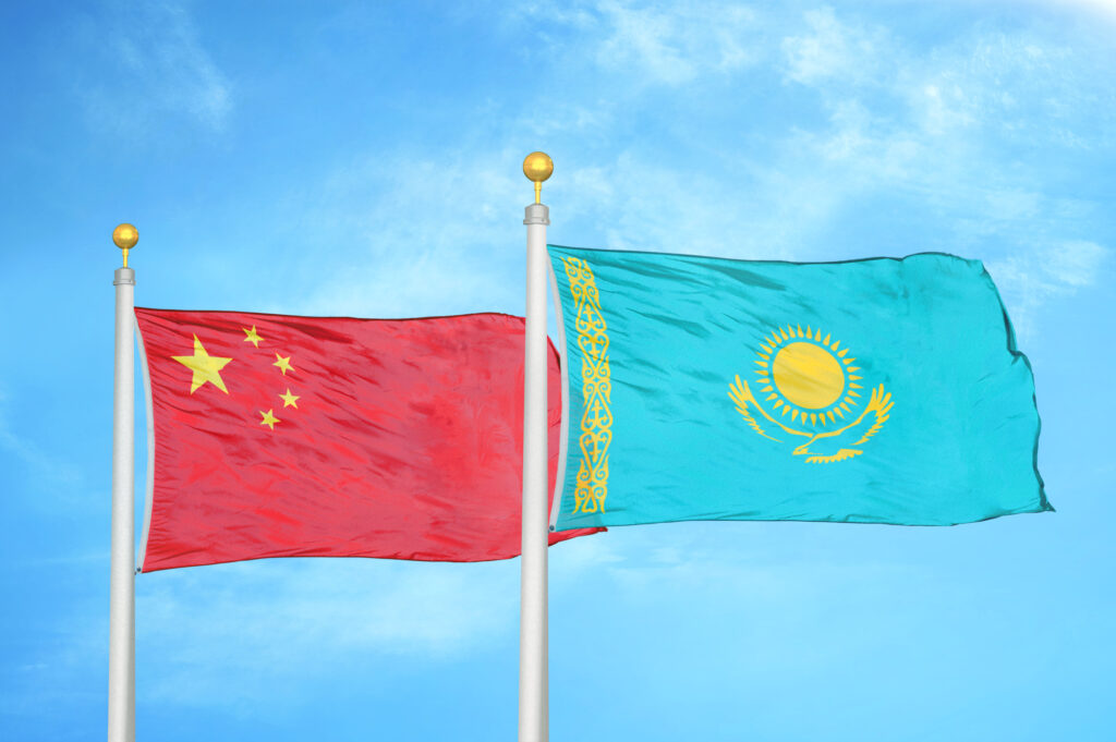 China and Kazakhstan two flags on flagpoles and blue cloudy sky background