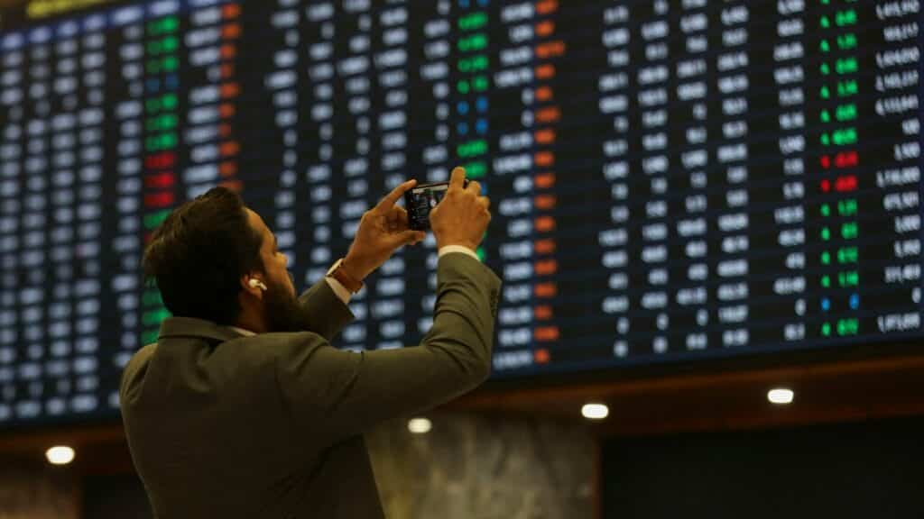 A man uses a mobile phone as he takes a photo of the electronic board displaying share prices during a trading session at the Pakistan Stock Exchange, in Karachi, Pakistan November 28, 2023. REUTERS/Akhtar Soomro