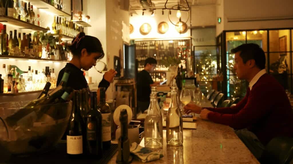 A staff member sniffs wine in a glass while a customer watches at Trio Wine Bar in Beijing, China November 1, 2023. REUTERS/Florence Lo