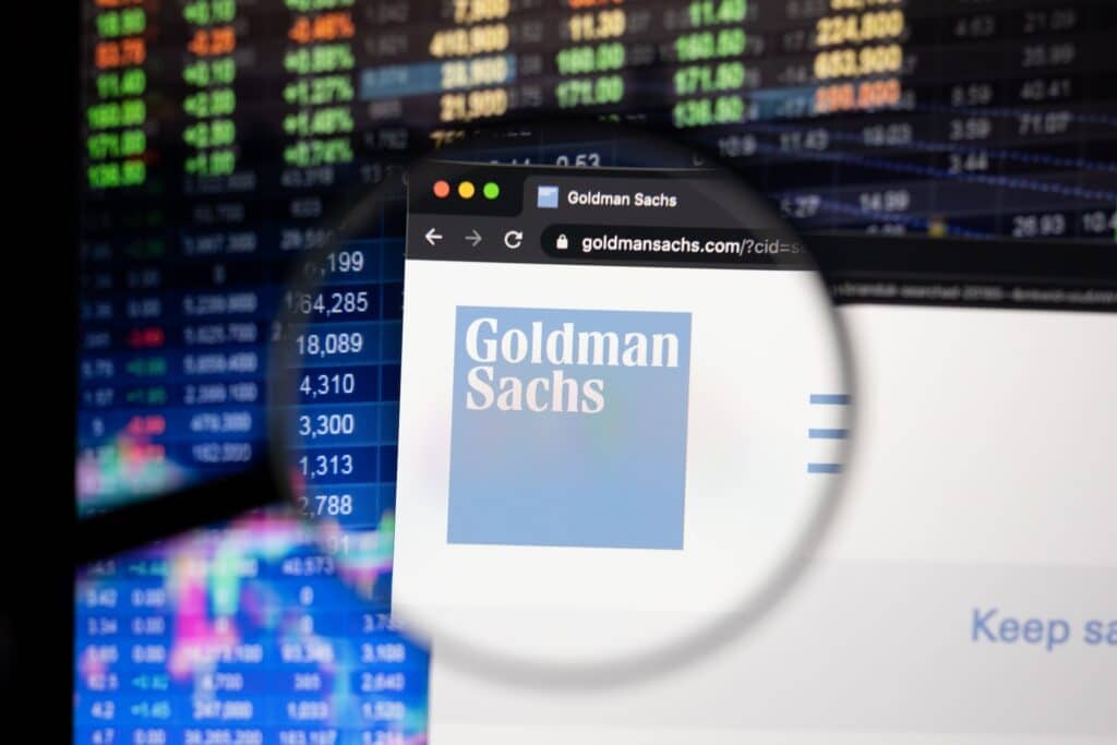 KAUFBEUREN, GERMANY - APRIL 26, 2021: Goldman Sachs company logo on a website with blurry stock market developments in the background, seen on a computer screen through a magnifying glass.