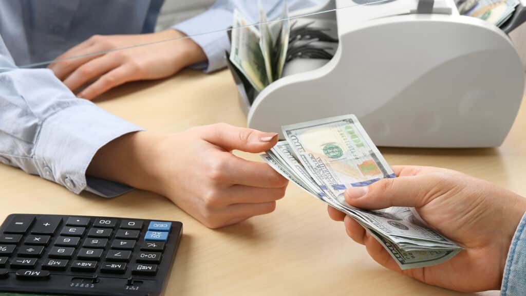 Client giving dollar banknotes to cashier at table in money exchange, closeup