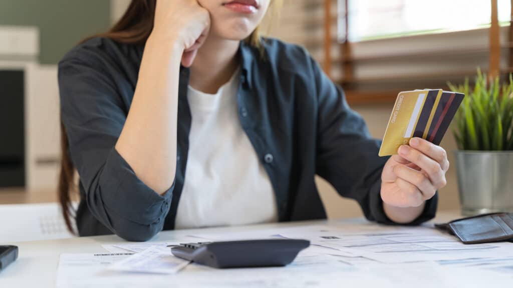 Sad Asian woman looking at many credit cards in her hand and worried about loan debt pay late.