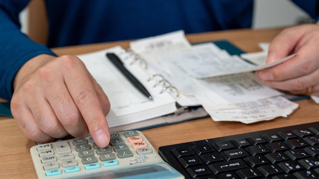 A man is writing a household ledger while organizing receipts. A close-up of hands. Tax or year-end settlement concept.