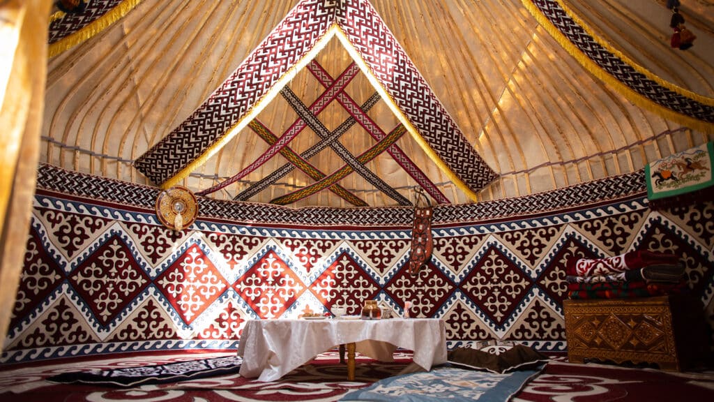 Interior of a Central Asian yurt with felt carpets, furniture, and a table. Traditional nomadic dwelling with white tablecloth.
