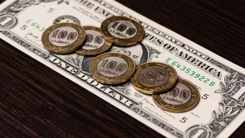Conceptual story about inflation and the US dollar exchange rate in Kazakhstan with six 100 Kazakhstani tenge coins and a 1 US dollar bill
