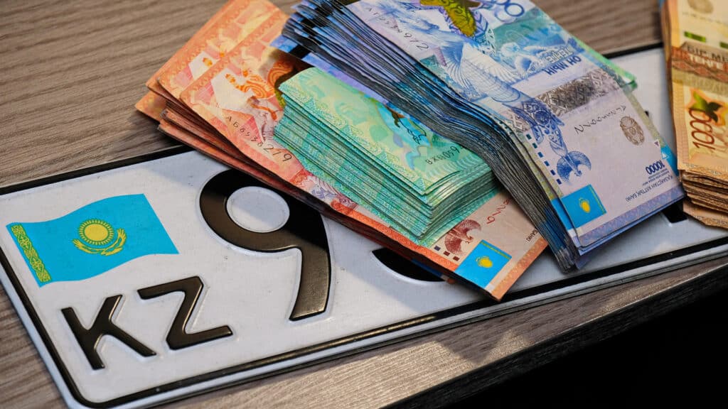 Almaty, Kazakhstan - 12.01.2020 : Banknotes of different denominations of Kazakhstani tenge are located on the car license plate with the symbol KZ