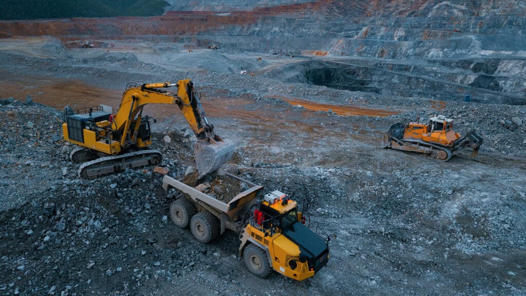 Heavy machinery operating in open pit mining at dusk with bulldozer and excavator loading of gold bearing ore.