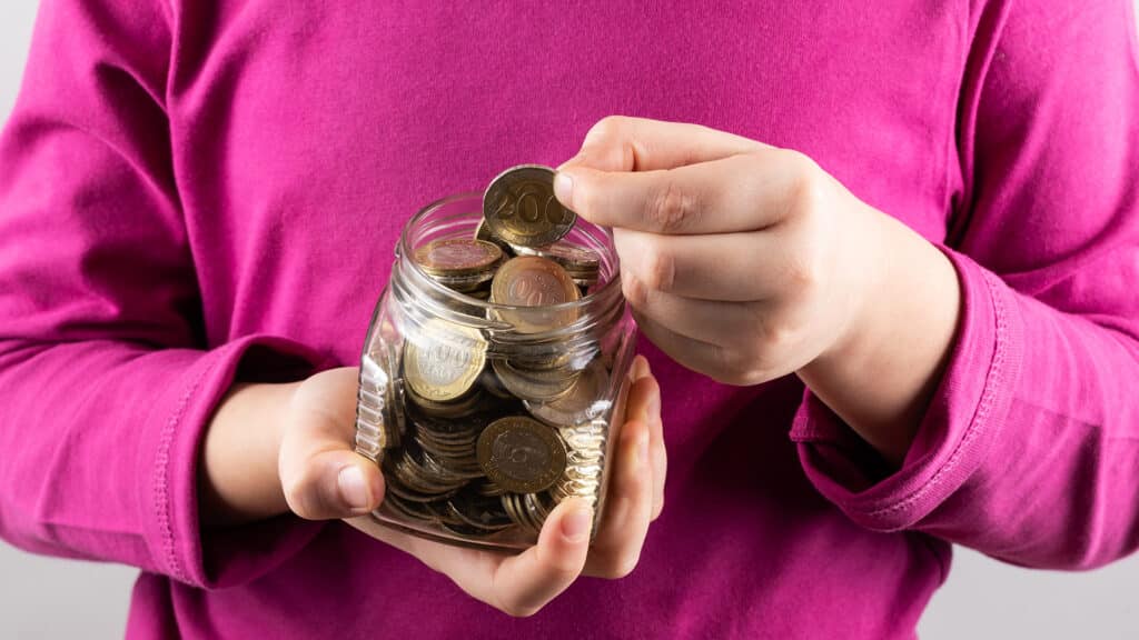 Glass jar with coins of 100 and 200 Kazakhstani tenge in children's hands