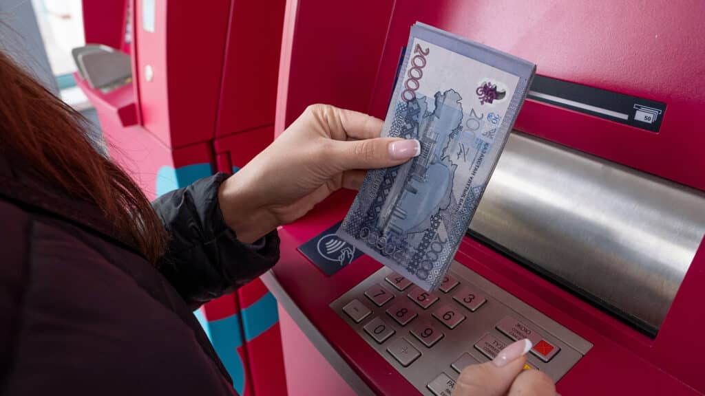 A large amount of money in a woman's hand against the background of an ATM. Kazakhstani tenge in women's hands. 20,000 banknotes of Kazakhstani tenge.