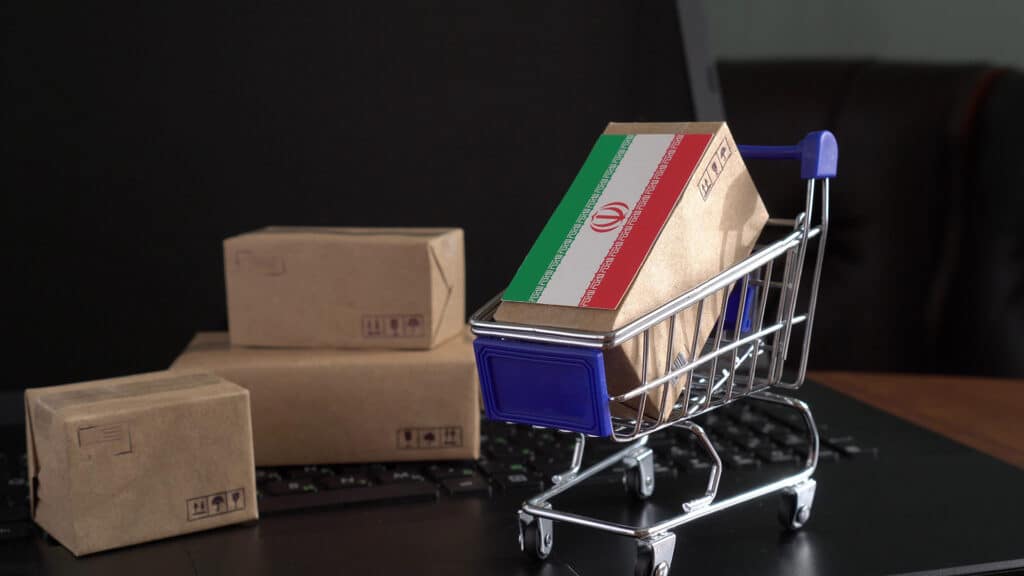 Parcel Boxes with a flag of Iran in a shopping cart on a laptop keyboard. Trade at an international level