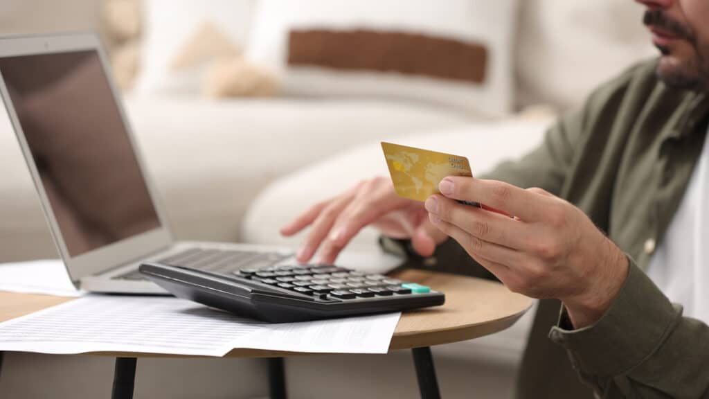 Man with laptop, calculator and credit card planning budget at table indoors, closeup. Debt problem