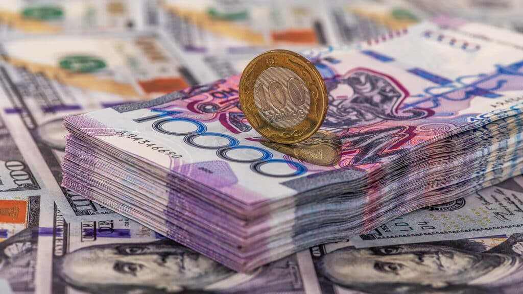 Banknotes of 10,000 Kazakhstani tenge and 100 tenge coin against the background of 100 US dollar bills