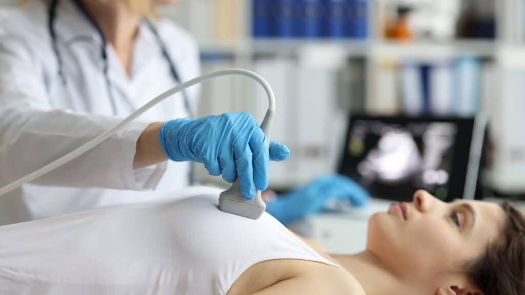 Portrait of doctor makes woman breast ultrasound, treatment before breast augmentation, full checkup in clinic. Womans health, medicine, hospital concept