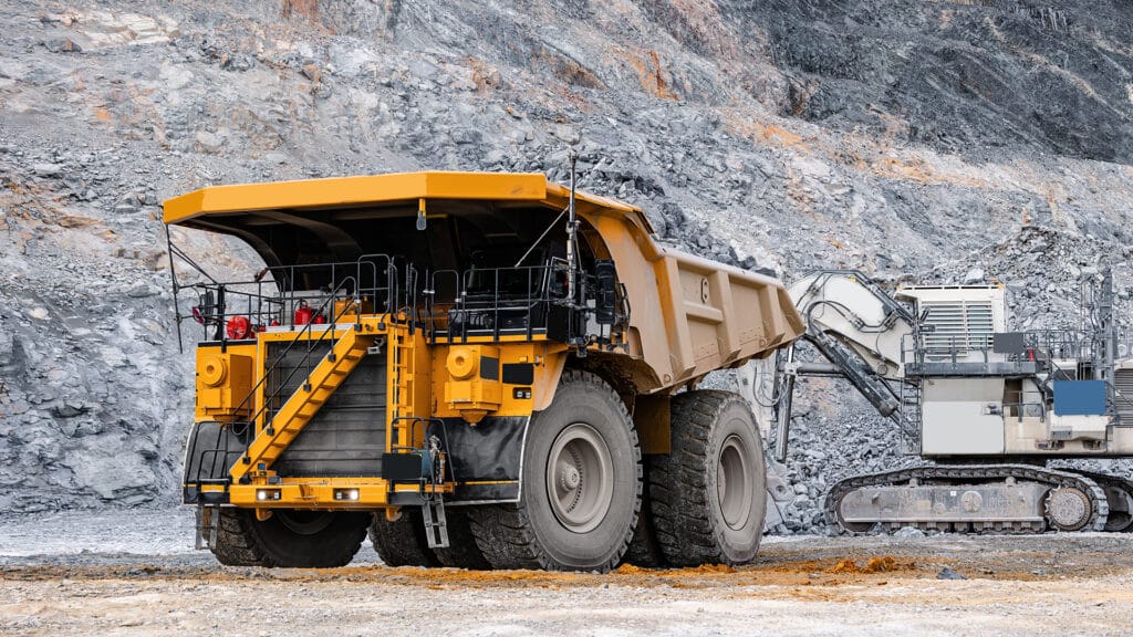 Heavy Mining Dump Truck with gold ore and Excavator at Open-Pit Mine.