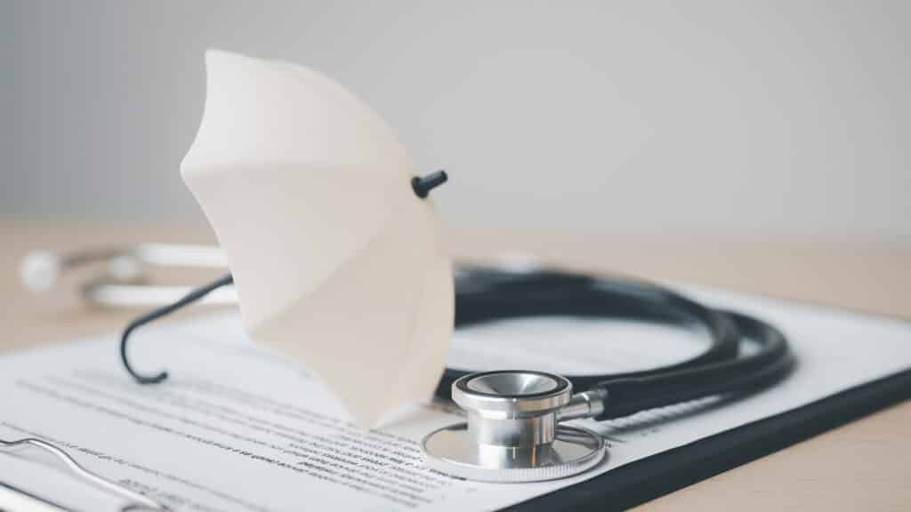 health, insurance, medical, policy, coverage, hospital, A stethoscope and a small umbrella placed on a health insurance document, symbolizing medical coverage, protection, and healthcare policy.