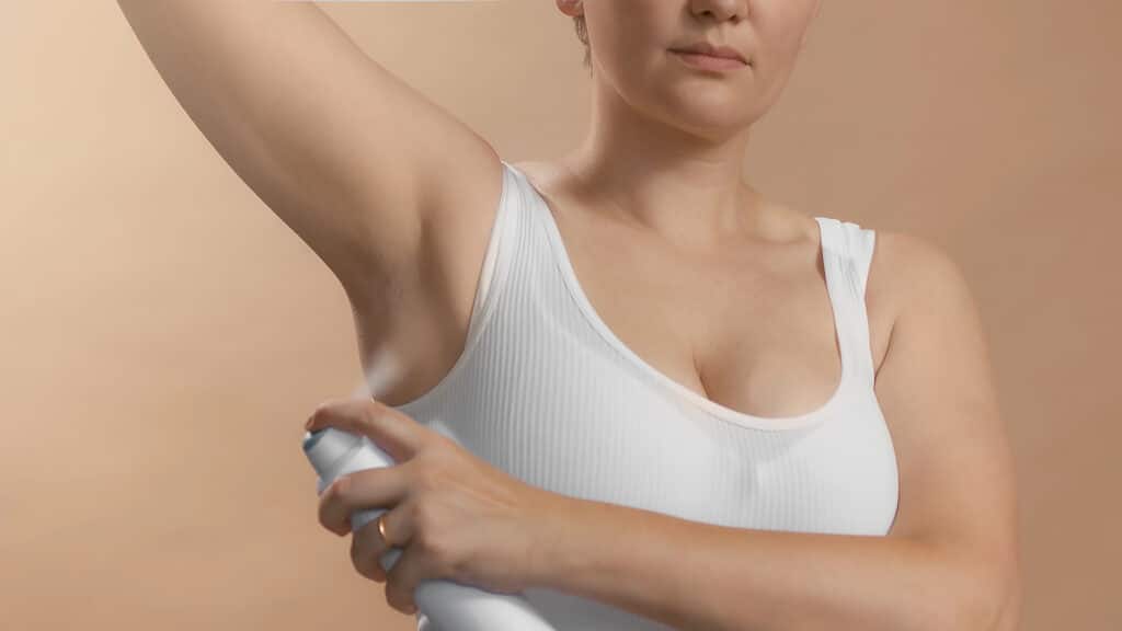 White young european female with lifted hand use antiperspirant to avoid stink and bad smelling. Clean seamless white bra. Studio high quality photo image on beige background.