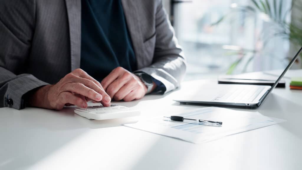 Businessman, hands or finance with calculator or documents for project budget or expenses in office. Man, accountant or tax collector with laptop for financial analysis, bills or audit in workplace