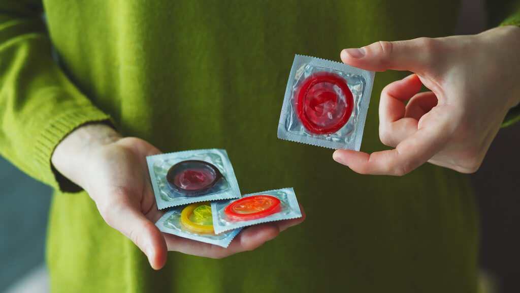 young woman holding red condom close up, hand with colorful condom packs, safe sex education concept, venereal diseases prevention