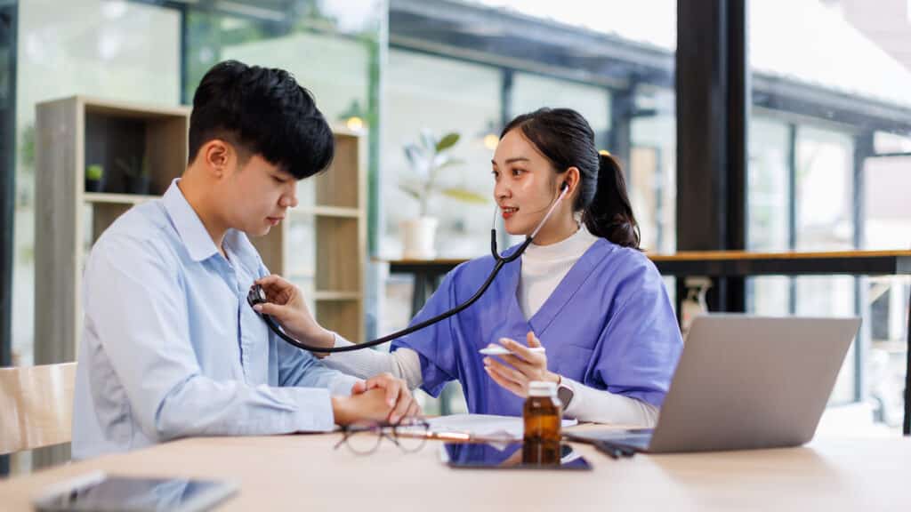 Asian woman nurse use stethoscope, checking up heart beat, lunch of auscultation in doctor office at hospital.Patient worker has to get medical checkup for her health or medical checkup cardiologist.