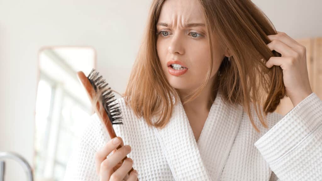 Worried young woman with hair loss problem and brush in bathroom, closeup