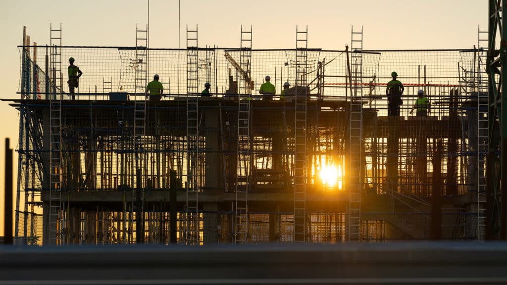 Construction workers on scaffolding making a formwork on a building site at sunset.