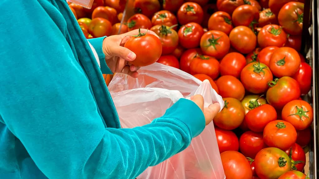 Woman using bio plastic bag while buying tomatoes at grocery store