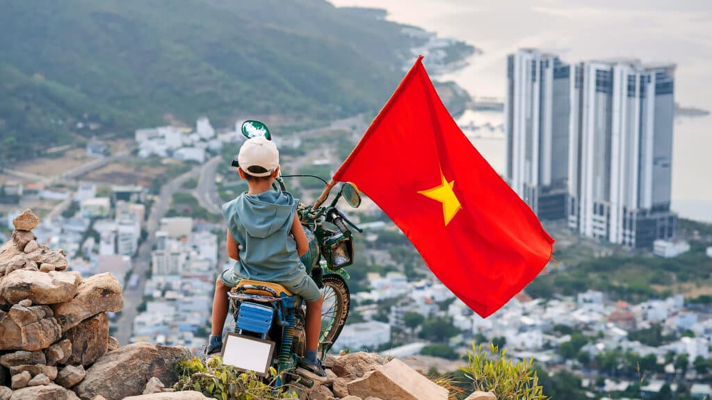 Back of tourist child boy on motorcycle on top of a mountain with a Vietnam flag. Mountain of Angels in Nha Trang in Vietnam