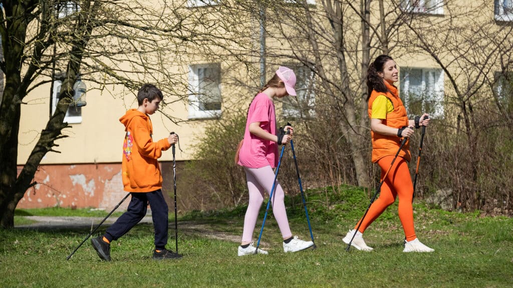 woman teaches children Nordic walking, sport walking with sticks, mother with children doing sports outdoors