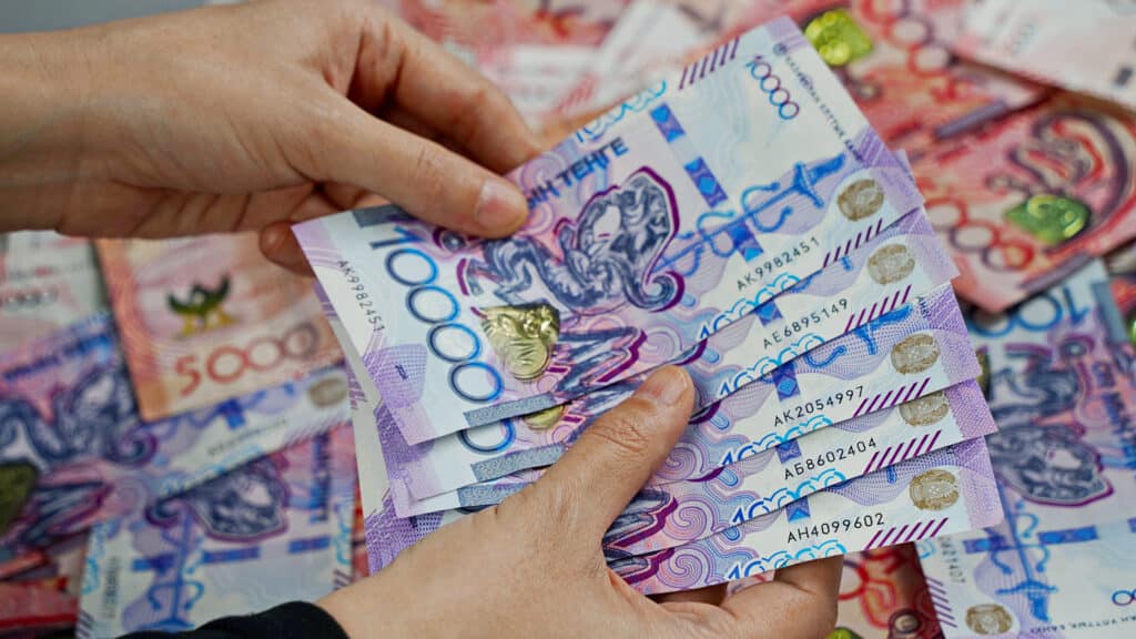 A woman collects and counts tenge banknotes in denominations of 5,000 and 10,000.
