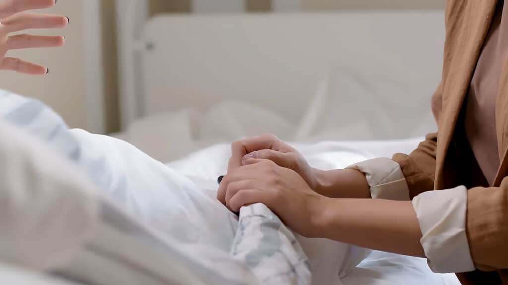 Caucasian daughter holding hand of tired mother patient lying in hospital bed