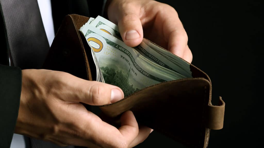 Man holding wallet with dollars on black background, closeup