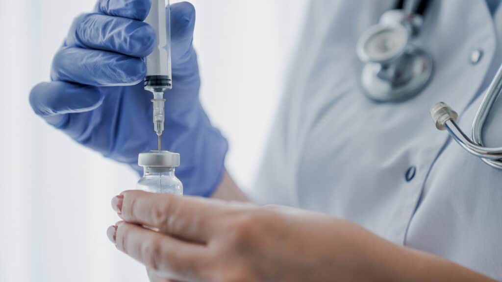 Close up of hands of doctor preparing for vaccination using ampule with remedy drug medicine for vaccination against viral infection, flu, influenza, coronavirus, tetanus, hepatitis, yellow fever