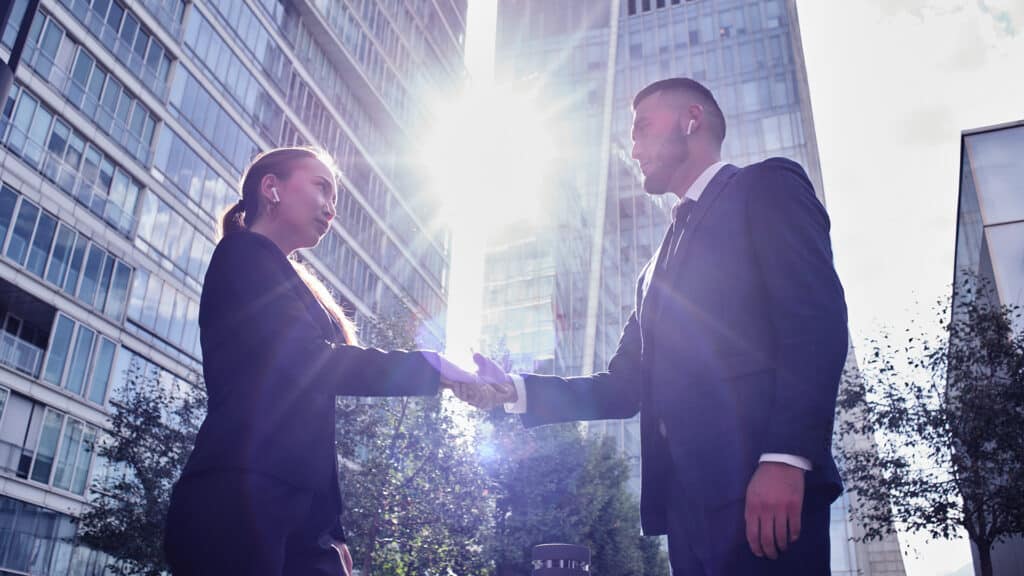 Asian Kazakh businessman and businesswoman meet and shake hands on the background of glass buildings of skyscrapers