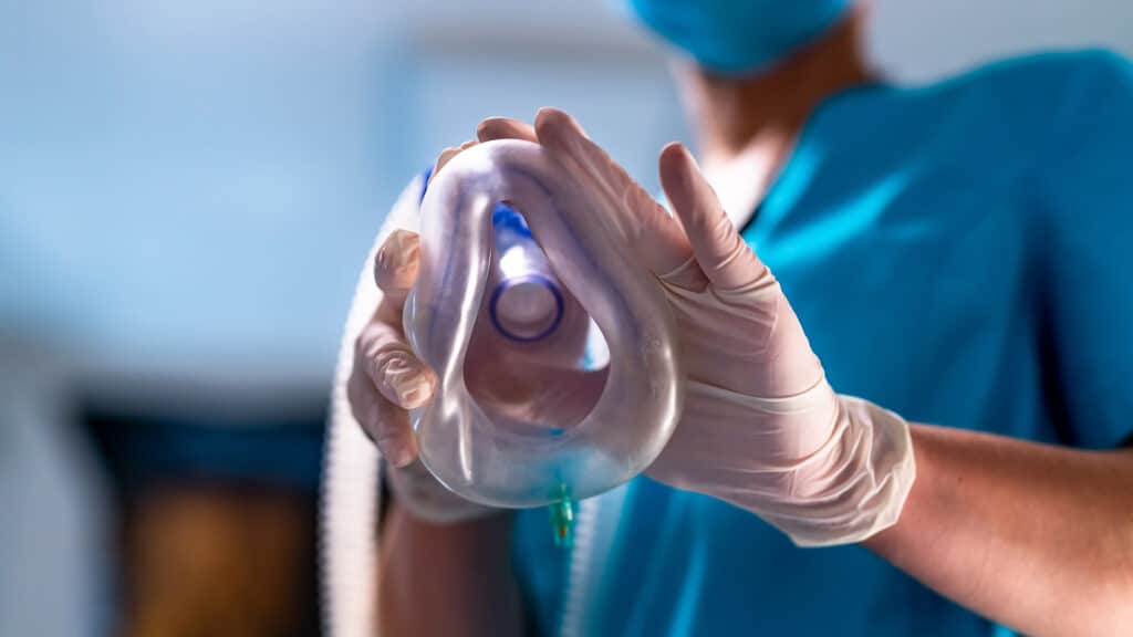 Anesthesia mask in hands. Gloved hands hold an anesthesia mask during clinical preparation.